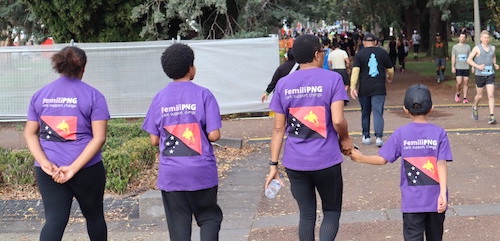 Four people walking in purple t-shirts with the Femili PNG logo and Papua New Guinea flag.